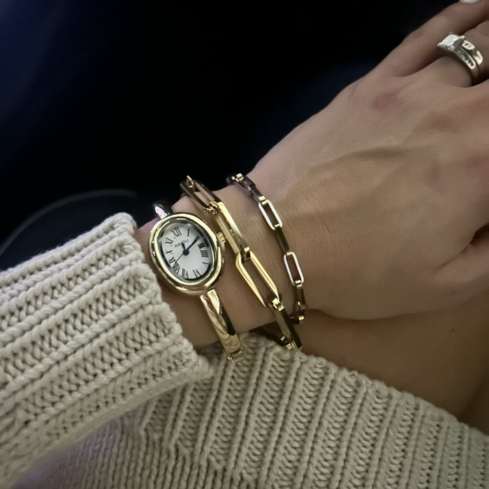 Wrist stack with a gold oval watch and paperclip chain bracelets