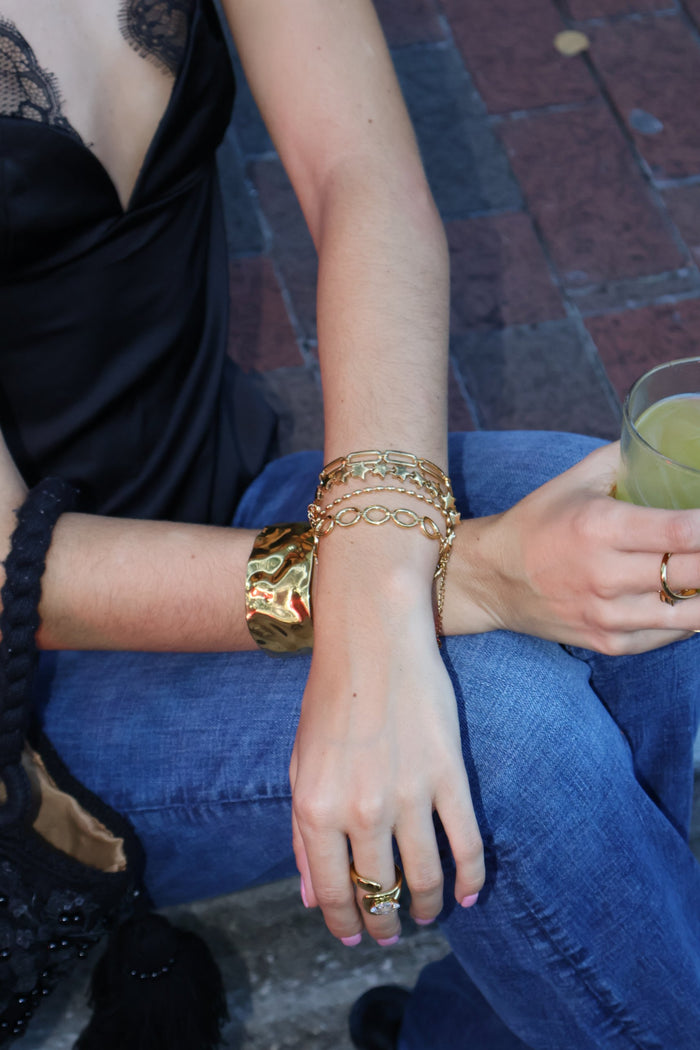 Stack of gold chain bracelets with a hammered gold cuff and rings worn on the wrist