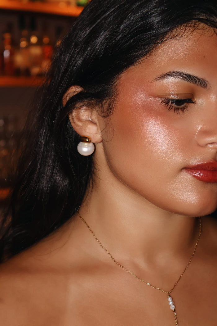 Gold and pearl statement stud earring worn with a dainty gold pearl necklace
