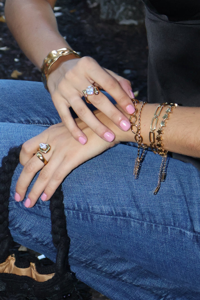 Hands wearing gold statement rings with crystal stones and stacked gold bracelets