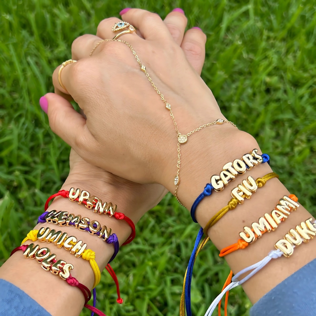 Two hands wearing colorful bracelets with text against a grass background