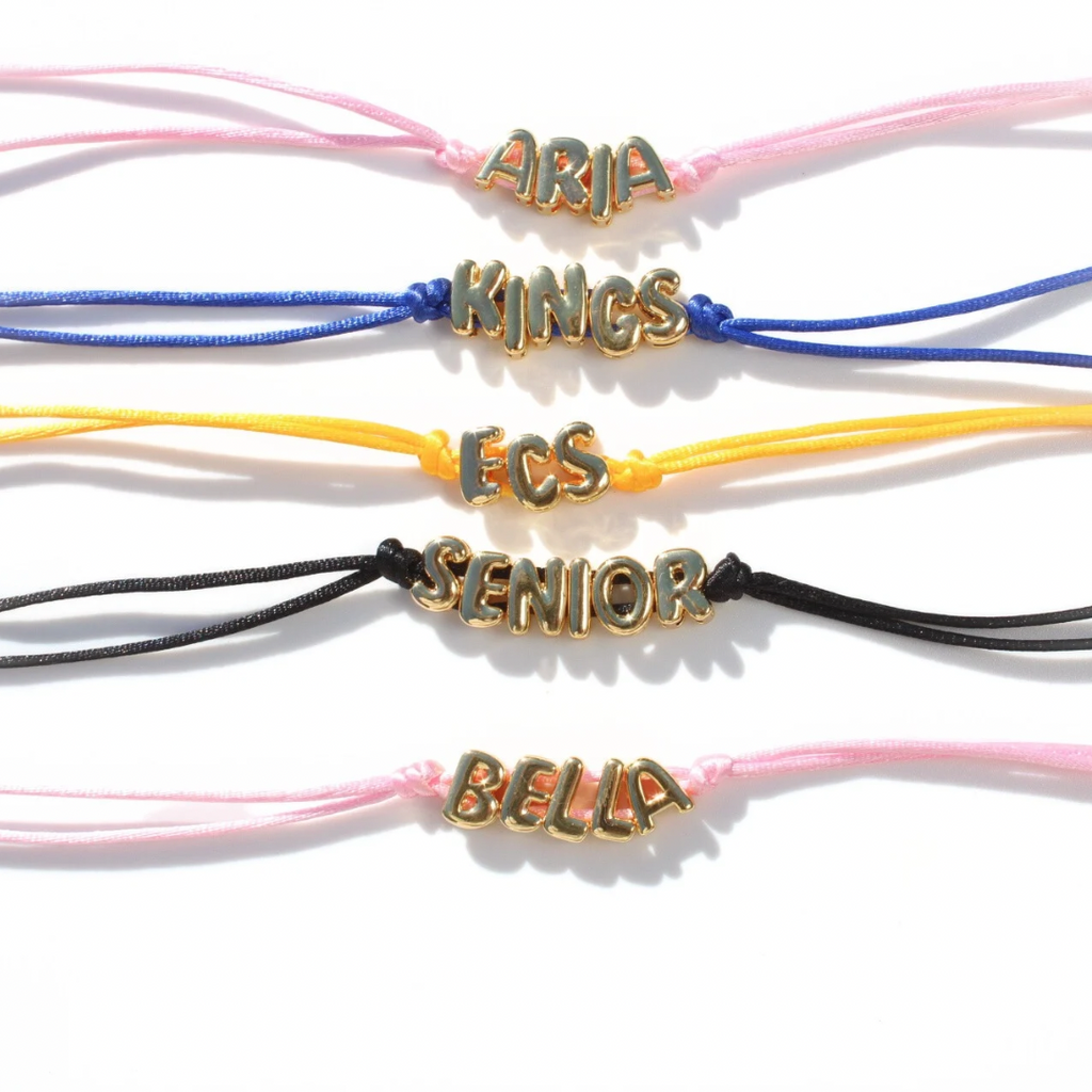 A collection of custom bubble letter bracelets in various colors, each featuring different names in capital letters.