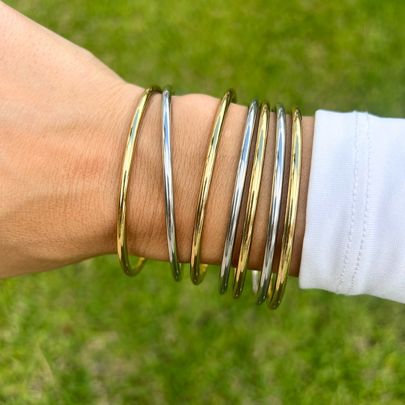 Set of seven mixed gold and silver plated stainless steel slim bangle bracelets stacked on wrist