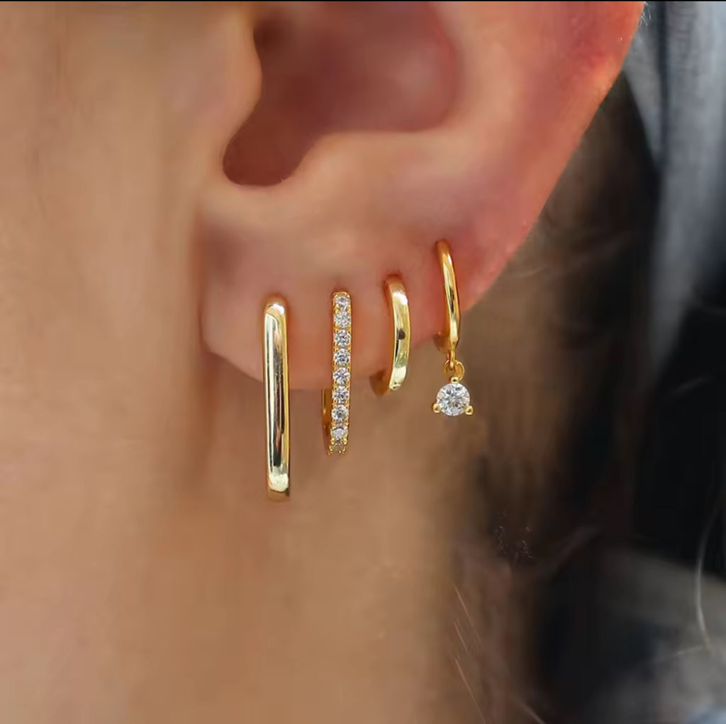 Close-up of an ear wearing gold hoop earrings with small gemstones.