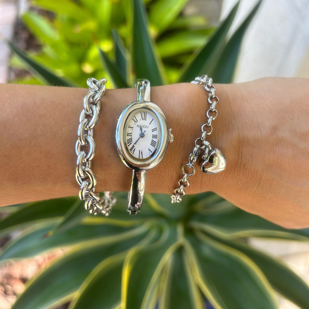 Silver watch with chain strap on a wrist against a green plant background