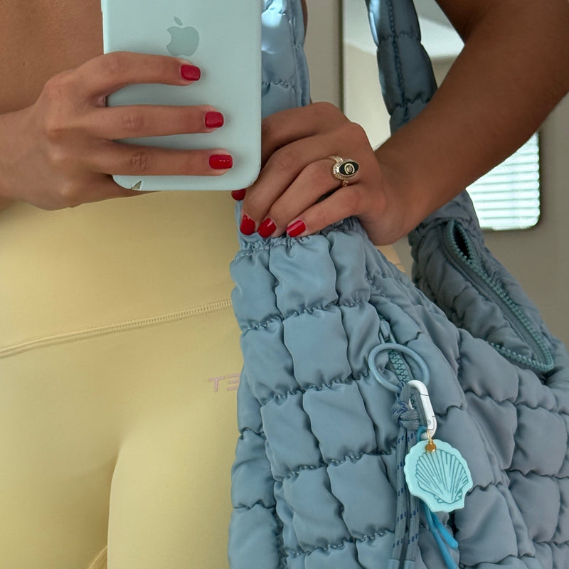 Blue acrylic seashell carabiner bag charm clipped onto white handbag